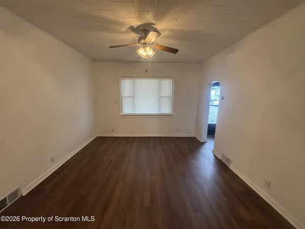 an empty room with wooden floor chandelier fan and windows