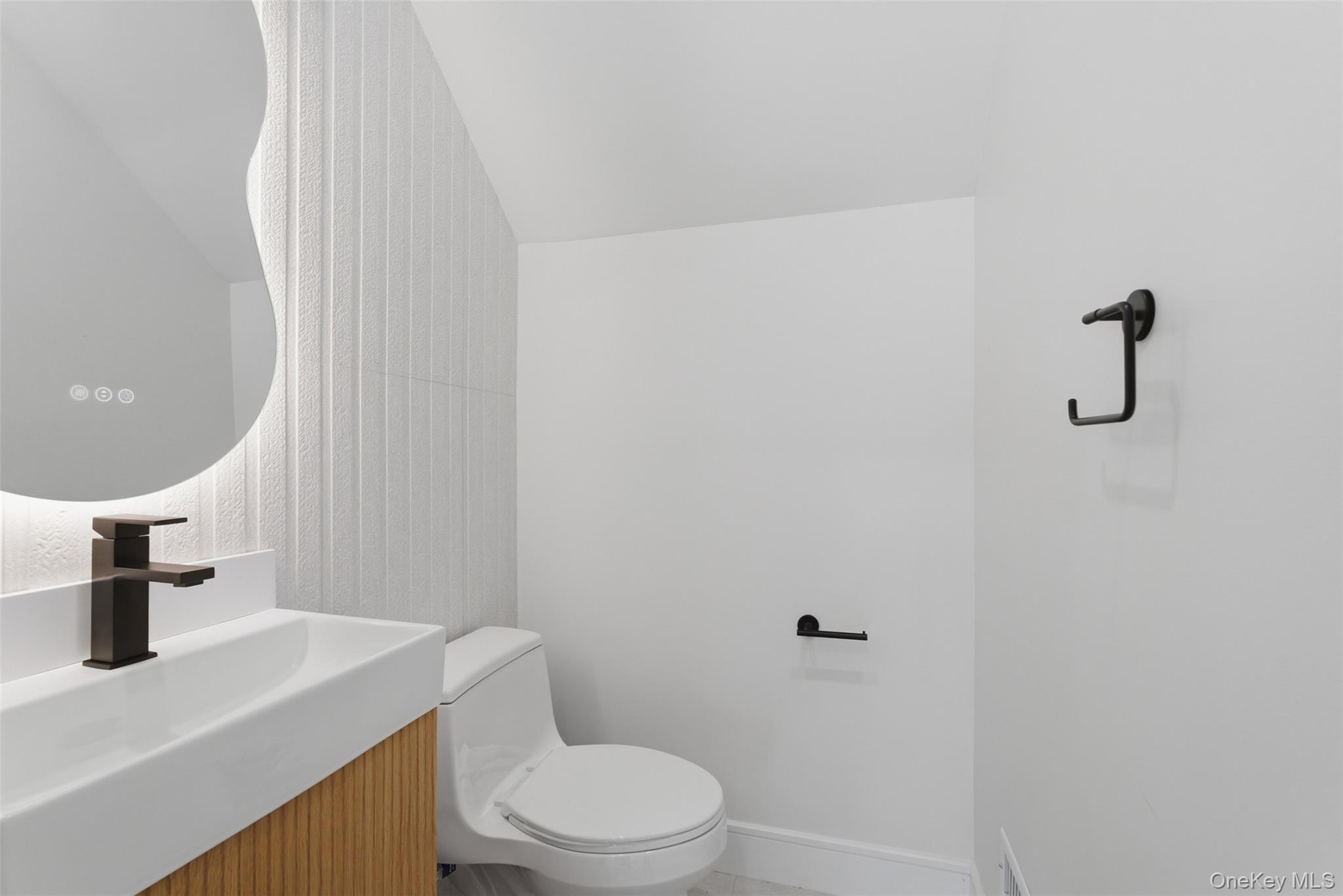 40 Calhoun Avenue New Rochelle, NY 10801 - Photo 10 of 49 Modern powder room featuring a white single-piece toilet, matte black fixtures, a wood-finish vanity with a rectangular basin, an illuminated frameless mirror, and a textured accent wall