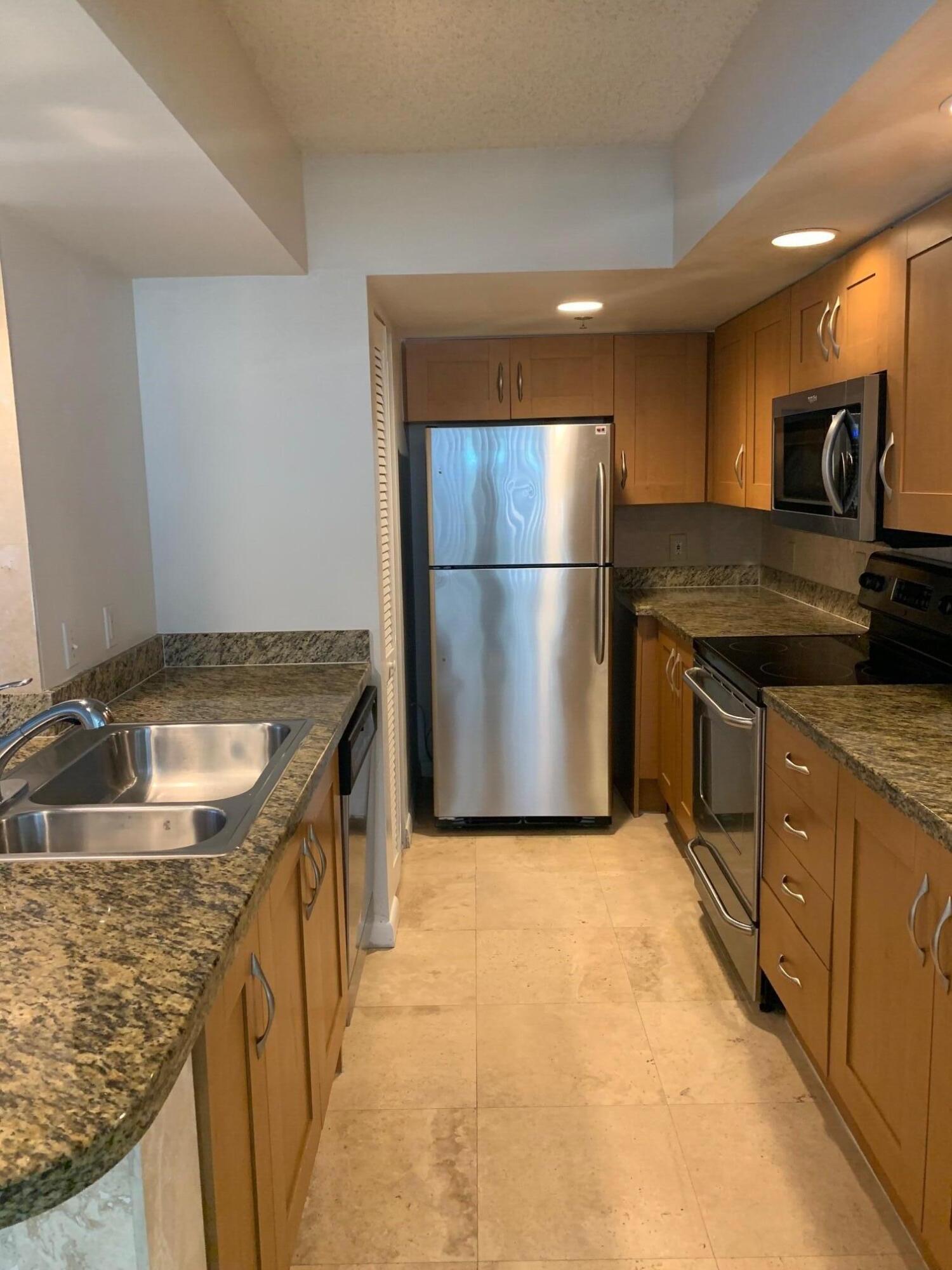 a kitchen with kitchen island granite countertop a sink and a refrigerator