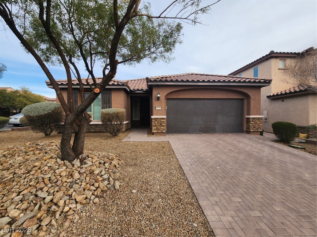 Mediterranean / spanish-style home featuring stone siding, stucco siding, a tile roof, decorative driveway, and a garage
