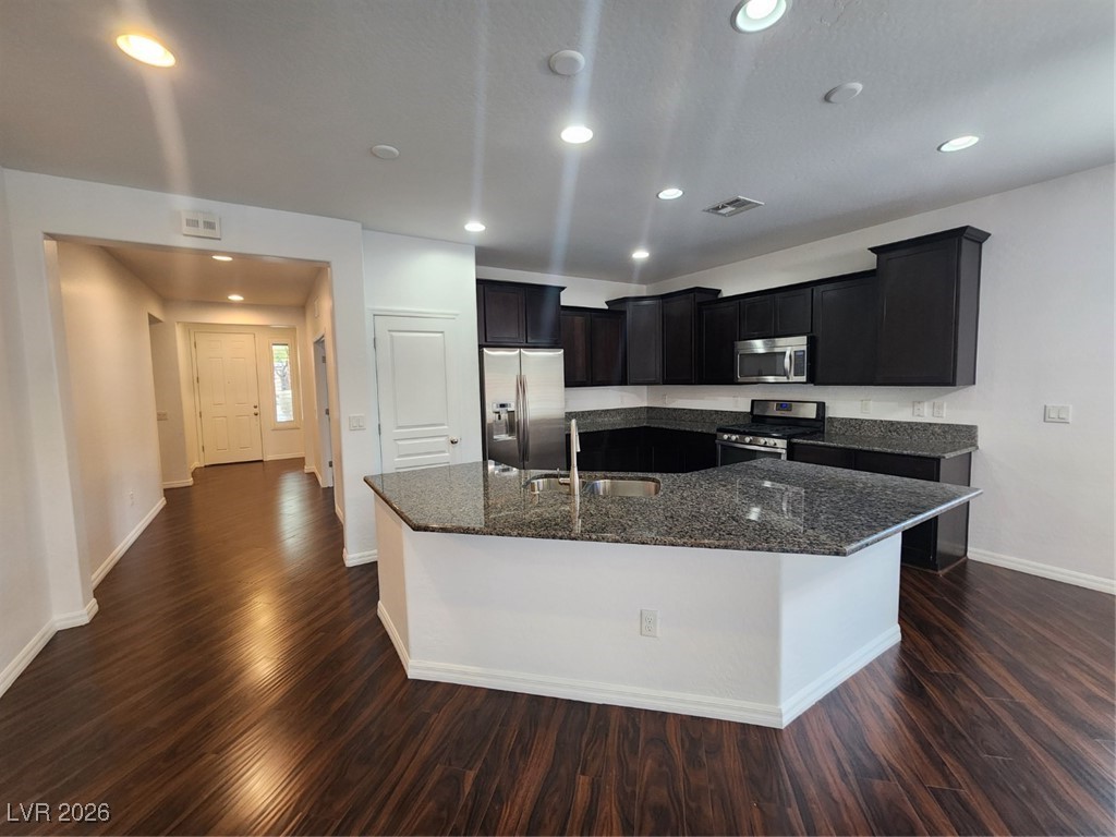 7022 Cordite Road Las Vegas, NV 89178 - Photo 6 of 51 Kitchen with dark stone countertops, white appliances, dark wood-type flooring, a kitchen island with sink, and recessed lighting