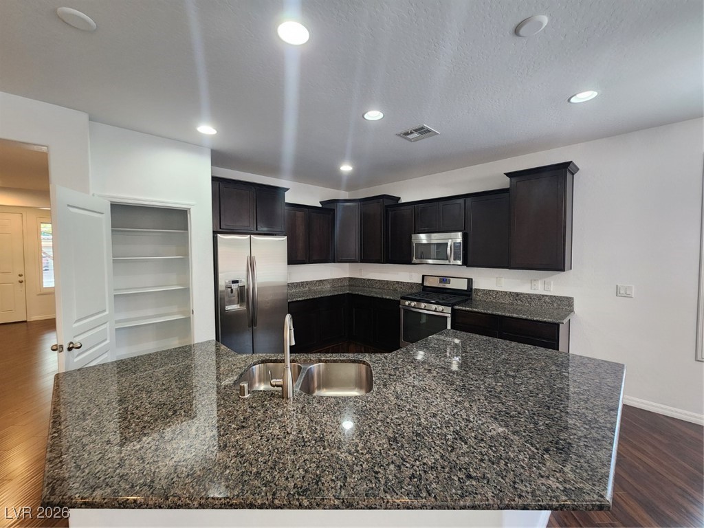 7022 Cordite Road Las Vegas, NV 89178 - Photo 7 of 51 Kitchen with dark wood-style flooring, stainless steel appliances, a center island with sink, dark stone countertops, and recessed lighting
