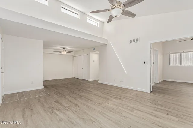 an empty room with wooden floor fan and windows