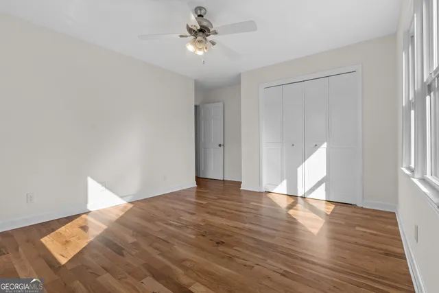 a view of an empty room with wooden floor and a ceiling fan