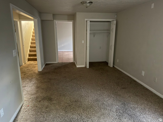 874 770 South Tooele, UT 84074 - Photo 5 of 19 Carpeted room with neutral wall paint, featuring a bi-fold closet with shelving, a hallway with stairs, and an additional doorway leading to a tiled area