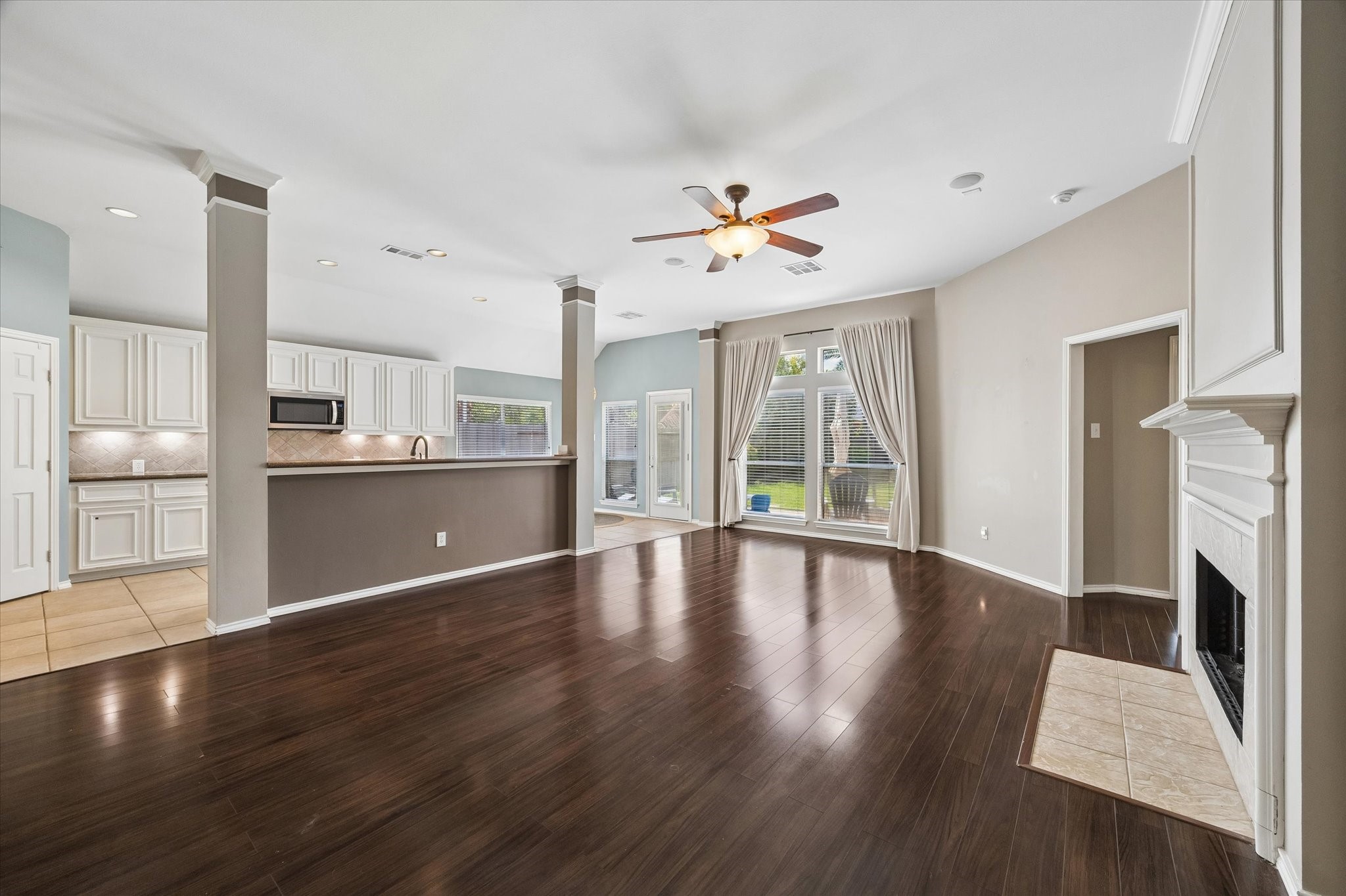 3118 Valley Court Manvel, TX 77578 - Photo 29 of 38 This spacious open-concept living area features a modern kitchen with white cabinetry, a cozy fireplace, and large windows offering plenty of natural light. The dark hardwood flooring and neutral wall colors create a warm and inviting atmosphere.