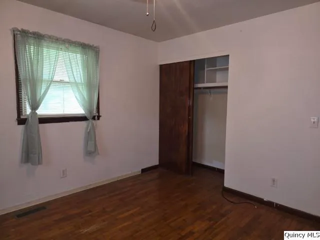 an empty room with wooden floor closet and windows