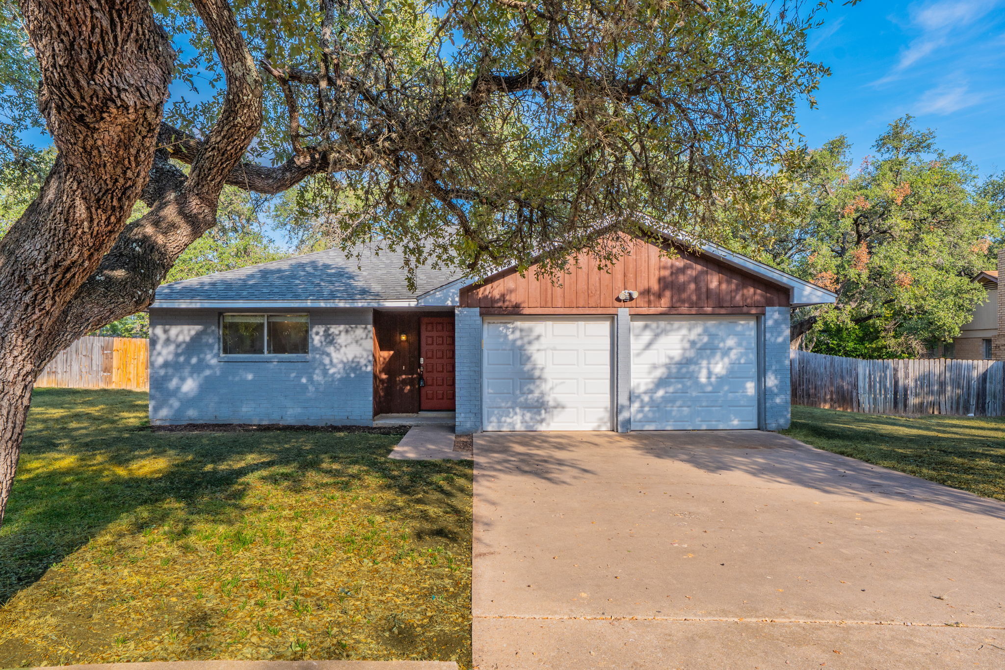 Mature shade trees frame the concrete driveway leading to a two-car garage.