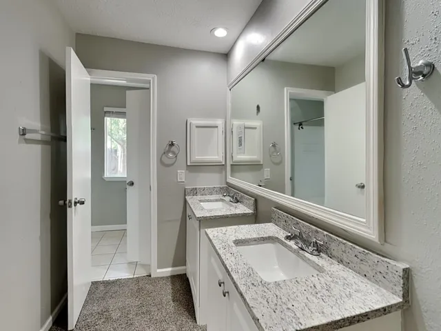 a bathroom with a granite countertop double vanity sink mirror and shower