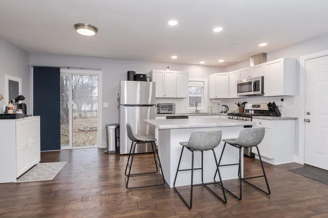 a kitchen with stainless steel appliances kitchen island granite countertop a refrigerator a stove a sink dishwasher and a dining table with wooden floor