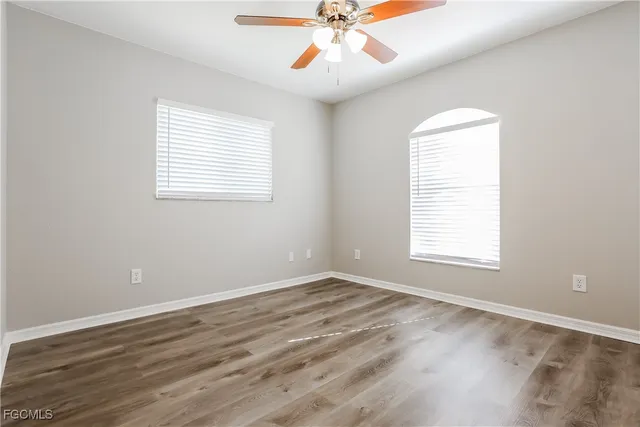 an empty room with wooden floor fan and windows