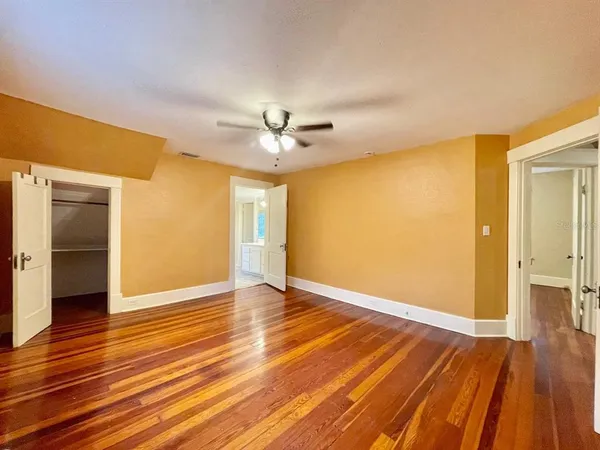 an empty room with wooden floor and a ceiling fan