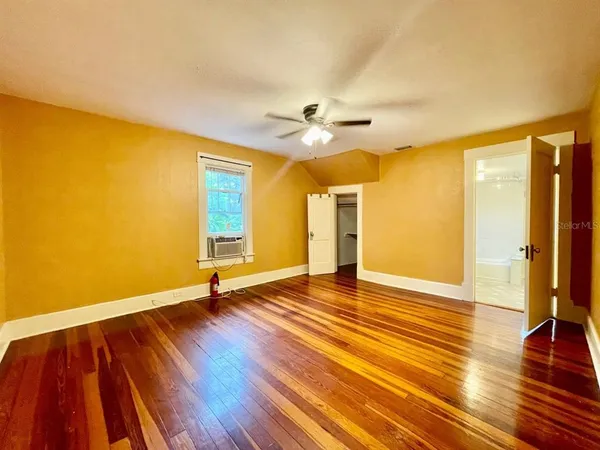 a view of an empty room with wooden floor and a ceiling fan