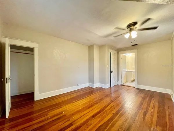 a view of an empty room with wooden floor and a ceiling fan