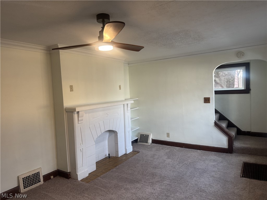 4058 Ardmore Road Cleveland, OH 44121 - Photo 3 of 14 Unfurnished living room with dark colored carpet, ornamental molding, a ceiling fan, a fireplace with flush hearth, and a textured ceiling
