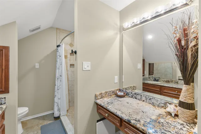 a bathroom with a granite countertop sink a toilet a mirror and shower