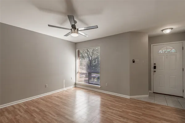 an empty room with wooden floor chandelier fan and windows