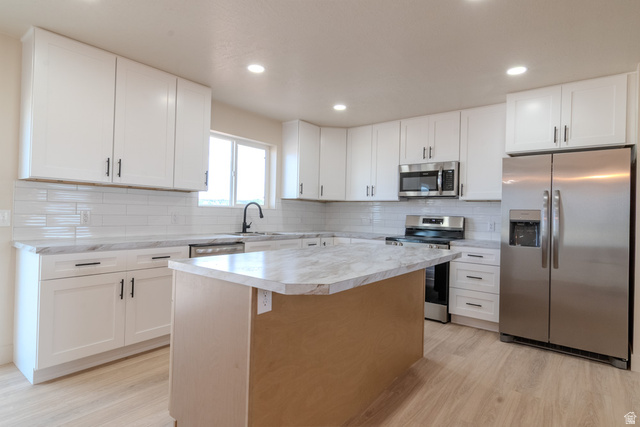 130 Pole Line Road, Unit 2 Roosevelt, UT 84066 - Photo 11 of 33 Modern kitchen featuring white cabinetry, light-toned countertops, stainless steel appliances, a center island, and wood-finish flooring