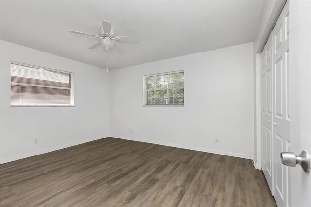 an empty room with wooden floor fan and windows