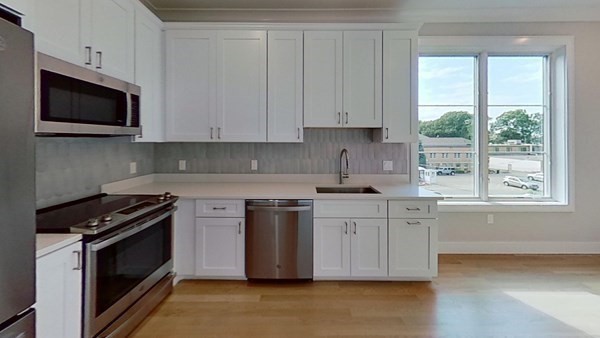 a kitchen with stainless steel appliances granite countertop white cabinets a sink a stove a microwave and wooden floors