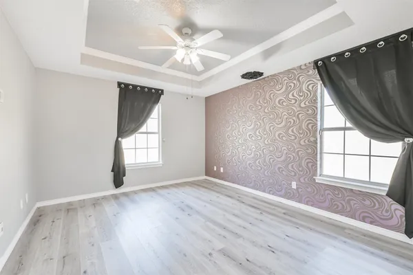 an empty room with wooden floor fan and windows