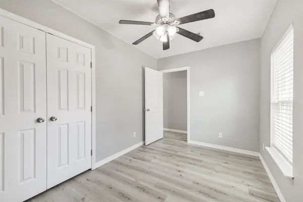 an empty room with wooden floor chandelier fan and windows
