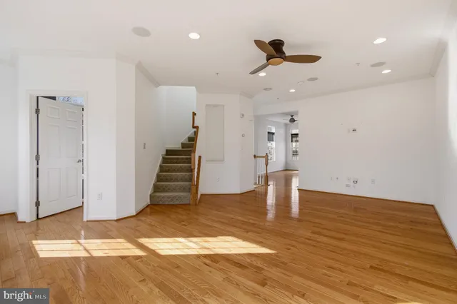 a view of an empty room with wooden floor and a ceiling fan