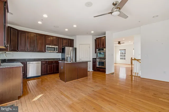a kitchen with stainless steel appliances kitchen island granite countertop a refrigerator a stove top oven and a sink with granite countertops
