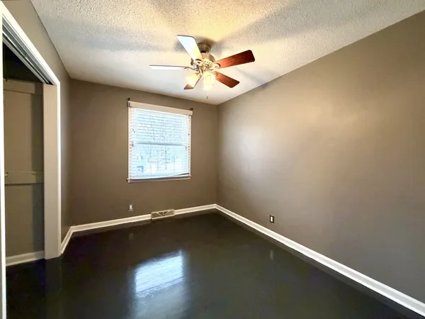 an empty room with wooden floor fan and windows