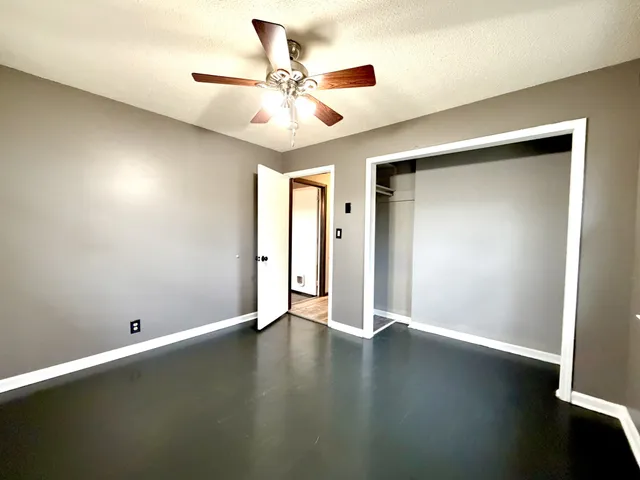 an empty room with wooden floor fan and windows