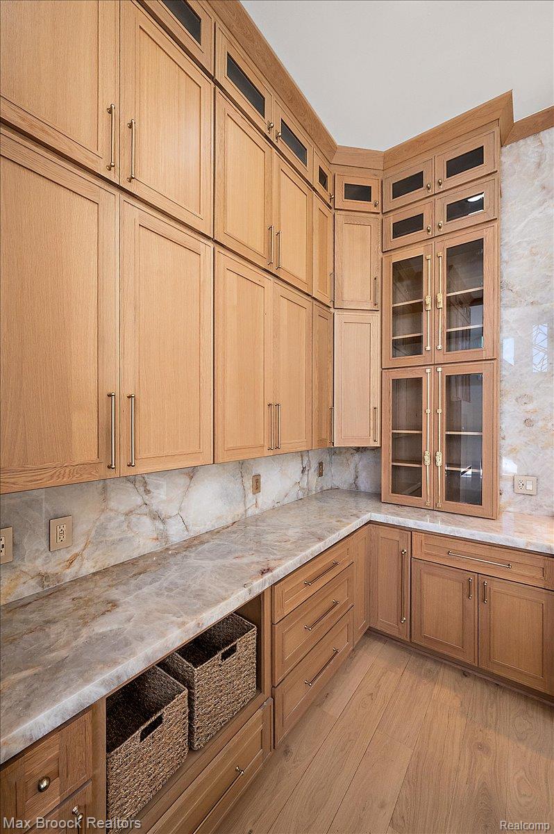 4597 Clarkston Road Clarkston, MI 48348 - Photo 22 of 74 Extensive light wood-finish cabinetry, stone slab countertops, stone slab backsplash, wood-finish flooring, and glass-front upper cabinets