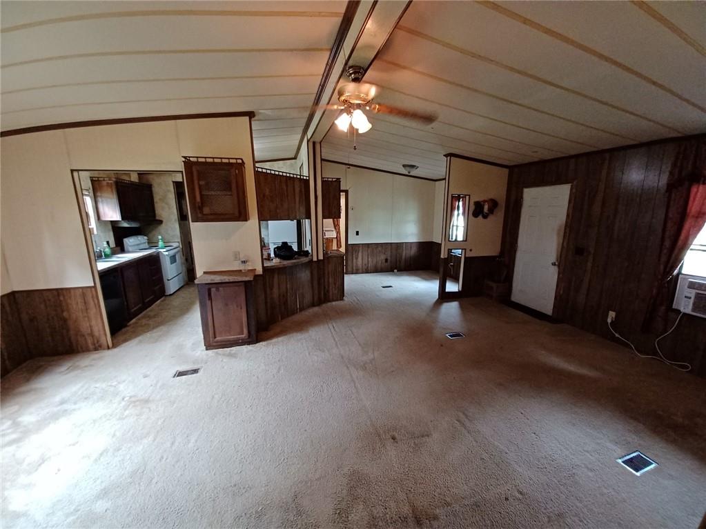 Kitchen featuring wooden walls, washer and clothes dryer, a ceiling fan, vaulted ceiling, and light colored carpet