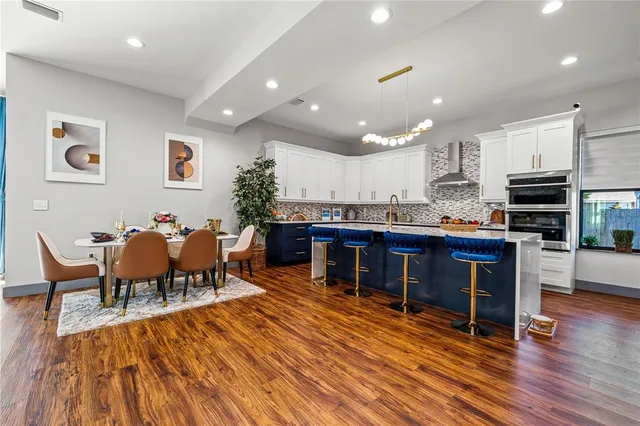a living room with stainless steel appliances furniture wooden floor and a kitchen view