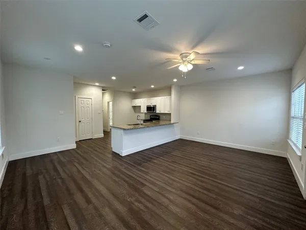 a view of an empty room with wooden floor and a ceiling fan