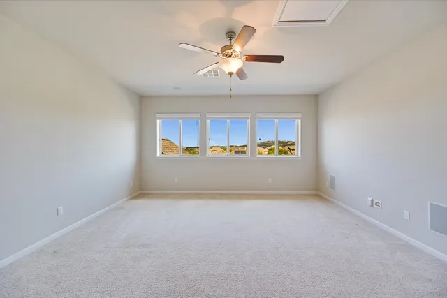 an empty room with chandelier fan and windows