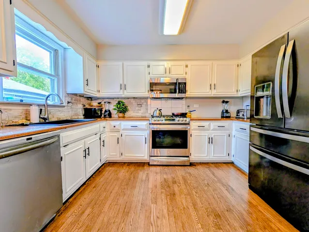 a kitchen with stainless steel appliances white cabinets a sink a stove a refrigerator and microwave with wooden floor