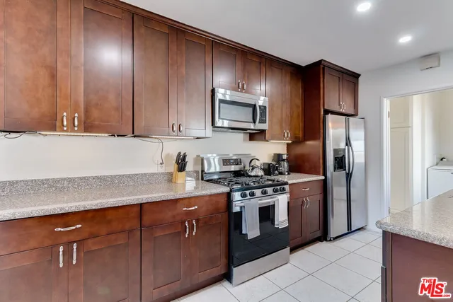 a kitchen with stainless steel appliances granite countertop a stove a refrigerator and a sink with wooden cabinets