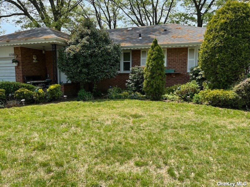 a view of a house with brick walls and a yard with plants and a large tree