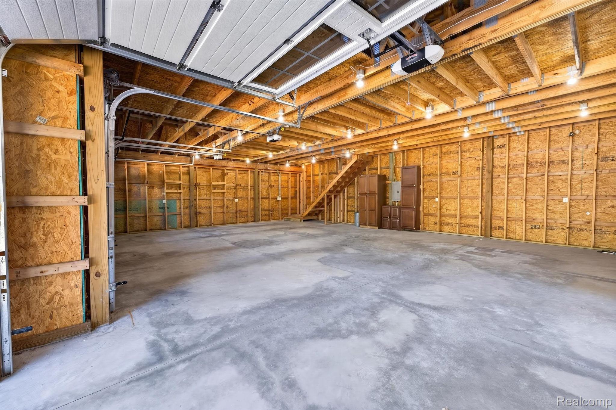 9353 Hill Road Swartz Creek, MI 48473 - Photo 69 of 98 Spacious garage featuring a concrete floor, exposed wood beam ceiling, multiple lighting fixtures, and a wooden staircase