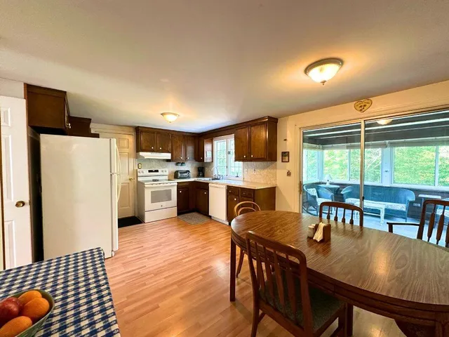 a open kitchen with stainless steel appliances granite countertop a refrigerator a stove a sink a dining table and chairs with wooden floor