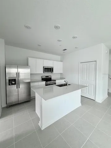 a large white kitchen with a sink a counter top space stainless steel appliances and cabinets
