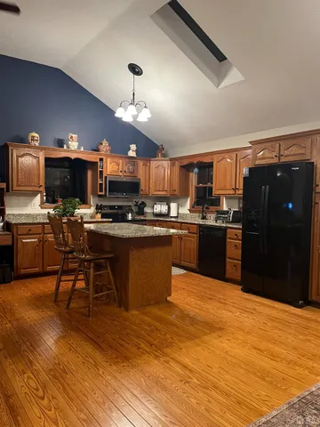 a kitchen with stainless steel appliances kitchen island granite countertop a refrigerator a stove top oven a sink dishwasher and wooden cabinets