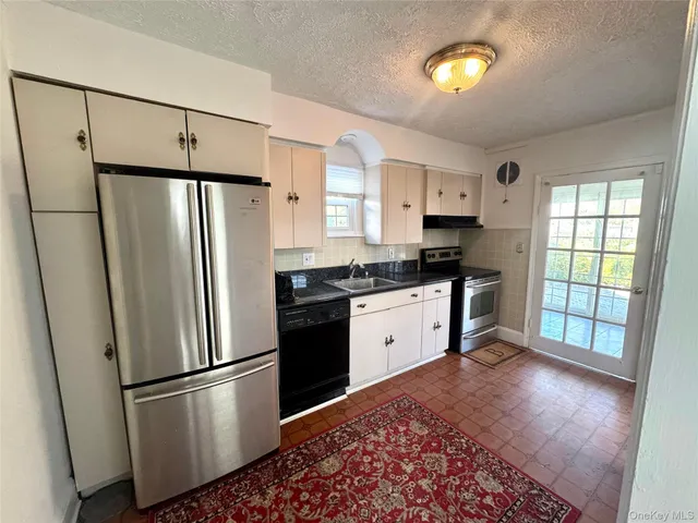 a kitchen with granite countertop a refrigerator a sink and white cabinets