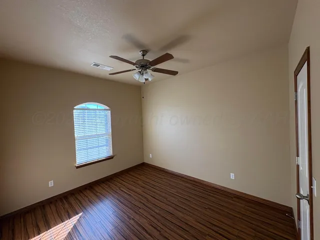 an empty room with wooden floor ceiling fan and windows
