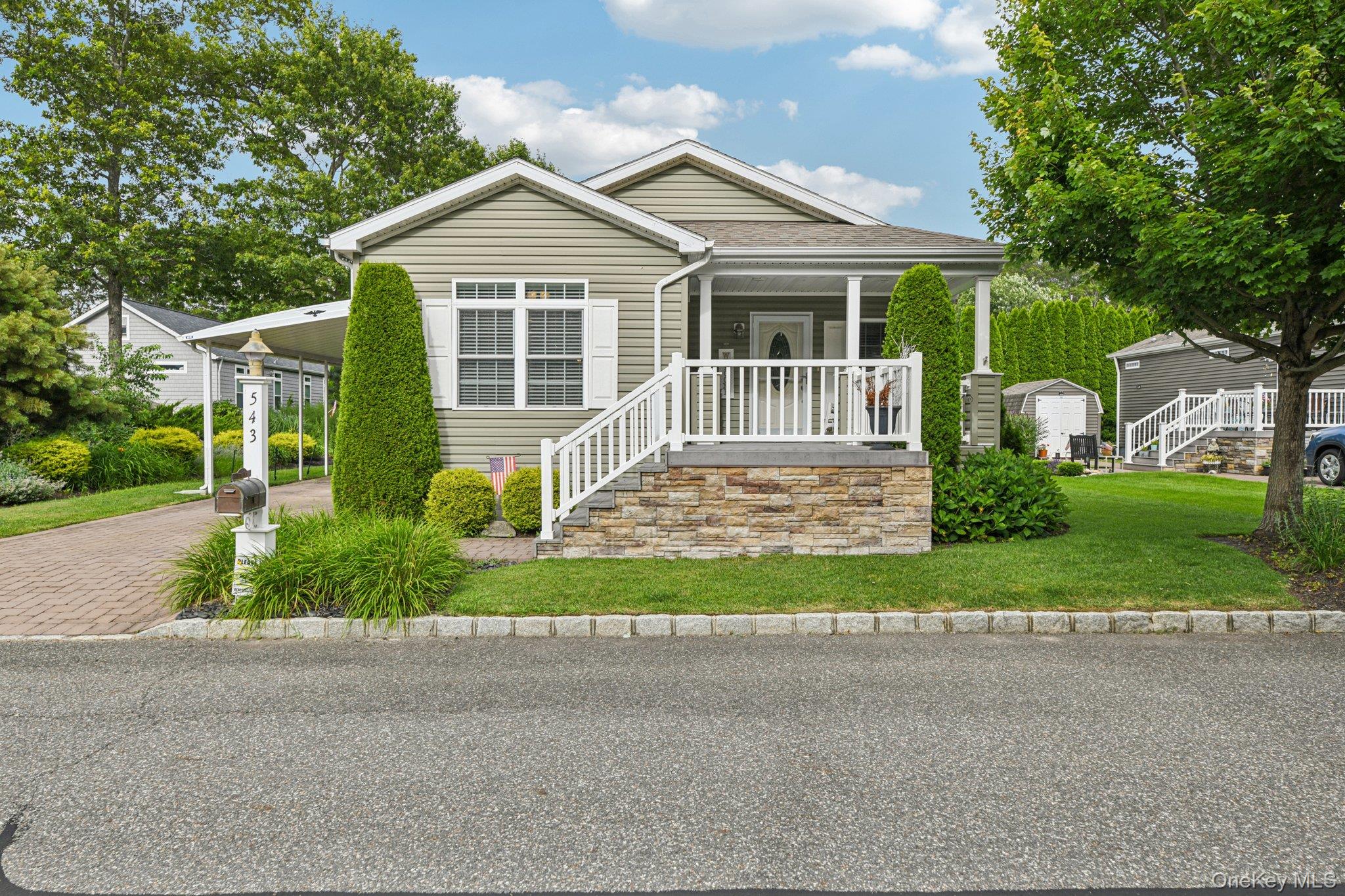 View of front of house featuring covered porch, decorative driveway, a front lawn, an attached carport, and stairs