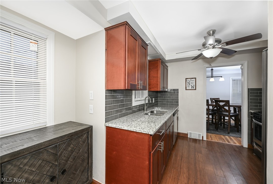 3699 Bainbridge Road Cleveland Heights, OH 44118 - Photo 15 of 37 Kitchen featuring wood-finish flooring, rich wood-tone cabinetry, a gray subway tile backsplash, light-toned granite-style countertops, and a ceiling fan with integrated lighting