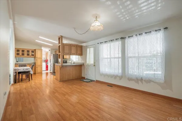 a living room with stainless steel appliances kitchen island granite countertop a stove a refrigerator a sink a dining table and chairs with wooden floor