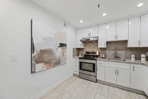 a kitchen with stainless steel appliances granite countertop white cabinets stove and a window