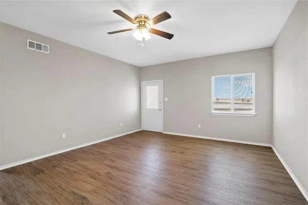 a view of an empty room with wooden floor and a ceiling fan