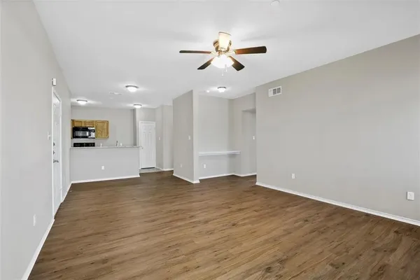 a view of an empty room with wooden floor and a ceiling fan